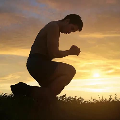 Pessoa ajoelhada com expressão de Agradecimento a Deus ao por do Sol
